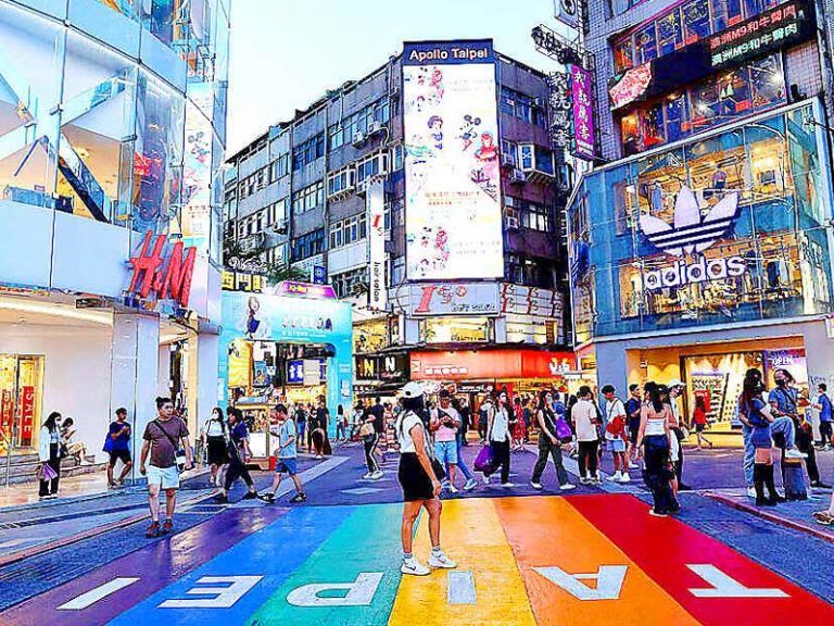 บรรยากาศย่านช้อปปิ้งซีเหมินติง ที่เที่ยวไต้หวันยอดฮิต ที่มีทางม้าลายสีรุ้งสดใสเป็นจุดเช็คอิน รายล้อมด้วยร้านค้าแบรนด์เนมและป้ายไฟนีออน