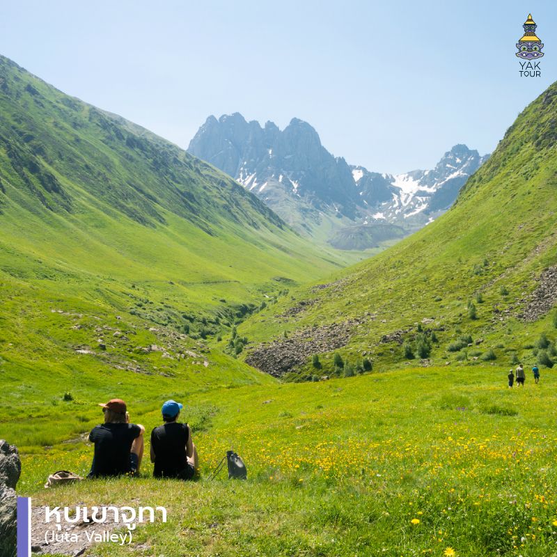 นักท่องเที่ยวนั่งชมวิวทุ่งหญ้าและยอดเขาหินแหลม Chaukhi ที่หุบเขาจูทา (Juta Valley) จอร์เจีย