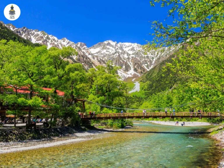 คามิโคจิช่วงฤดูใบไม้ผลิแสดงบรรยากาศสะพานไม้คัปปะบาชิและยอดเขาที่มีหิมะปกคลุม