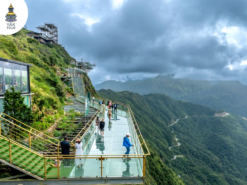 ทางเดินกระจกใส สะพานแก้วมังกรเมฆ (Rong May Glass Bridge) ที่ยื่นออกมาจากหน้าผาสูงชันบนยอดเขา O Quy Ho มองเห็นวิวทิวเขาและถนนคดเคี้ยวเบื้องล่างท่ามกลางม่านหมอก