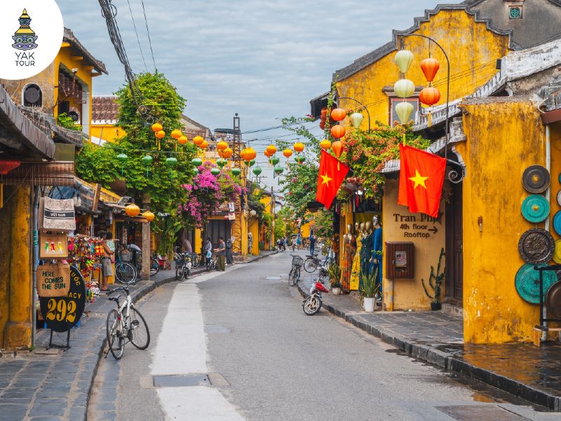 ตึกแถวโบราณสีเหลืองมัสตาร์ดประดับด้วยโคมไฟหลากสีและธงชาติเวียดนามในย่านเมืองเก่าฮอยอัน