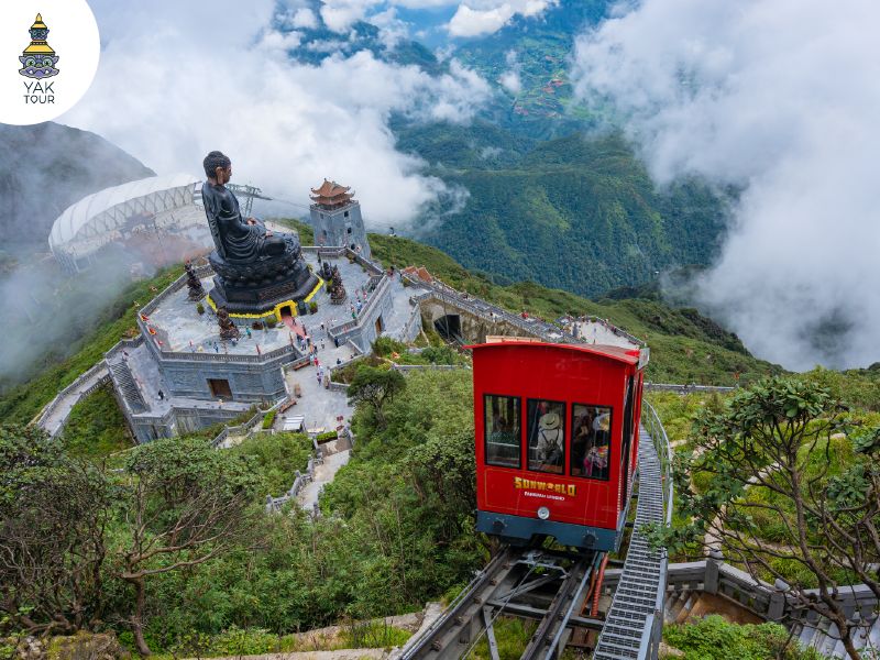 ทัศนียภาพบนยอดเขาฟานซิปัน (Fansipan) มองเห็นรถไฟไต่เขาขบวนสีแดงวิ่งมุ่งหน้าสู่ลานพระพุทธรูปองค์ใหญ่ท่ามกลางม่านหมอกและทิวเขาเขียวขจีในเมืองซาปา