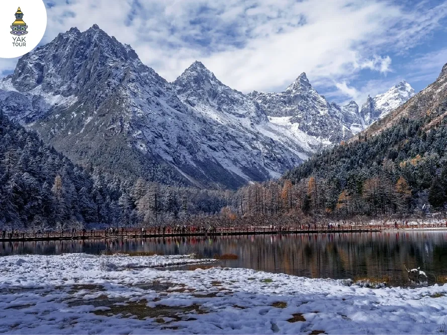 วิวสะพานไม้ทอดยาวผ่านทะเลสาบโดยมีฉากหลังเป็นเทือกเขาหิมะสูงชันในปี้เผิงโกว
