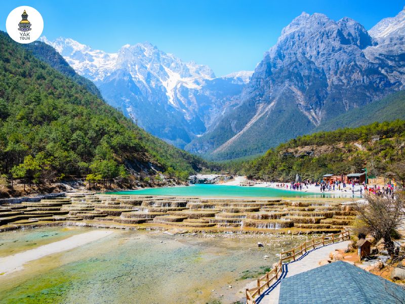 น้ำตกหินปูนชั้นเล็กๆ ในหุบเขาพระจันทร์สีเงิน ทะเลสาบสีฟ้าใสโอบล้อมด้วยป่าสนและยอดเขาหิมะ