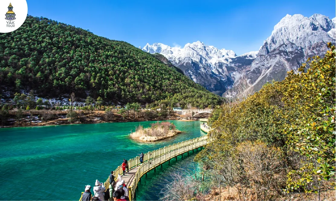 ทัศนียภาพหุบเขาพระจันทร์สีน้ำเงิน Blue Moon Valley ลี่เจียง น้ำใสสีเทอร์ควอยซ์และทางเดินไม้ริมทะเลสาบ มีฉากหลังเป็นภูเขาหิมะมังกรหยก