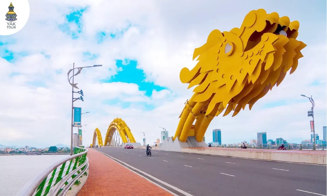 สะพานมังกร (Dragon River Bridge) ดานัง แสดงโครงสร้างหัวมังกรสีทองขนาดใหญ่และลำตัวทอดข้ามแม่น้ำฮัน ท่ามกลางบรรยากาศเมืองและท้องฟ้าสดใส