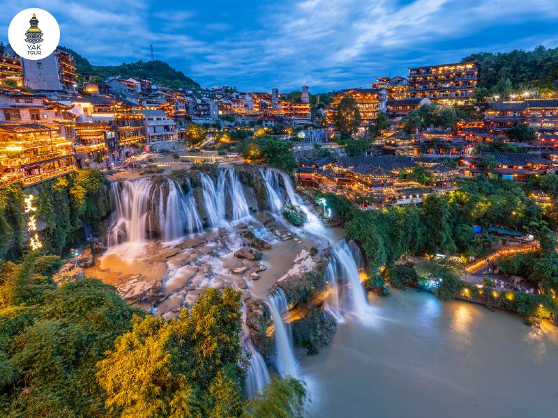 สถาปัตยกรรมไม้โบราณของหมู่บ้านฝูหรงเจิ้นบนหน้าผาสูงชันที่มีน้ำตกขนาดใหญ่ไหลผ่านใจกลางเมือง