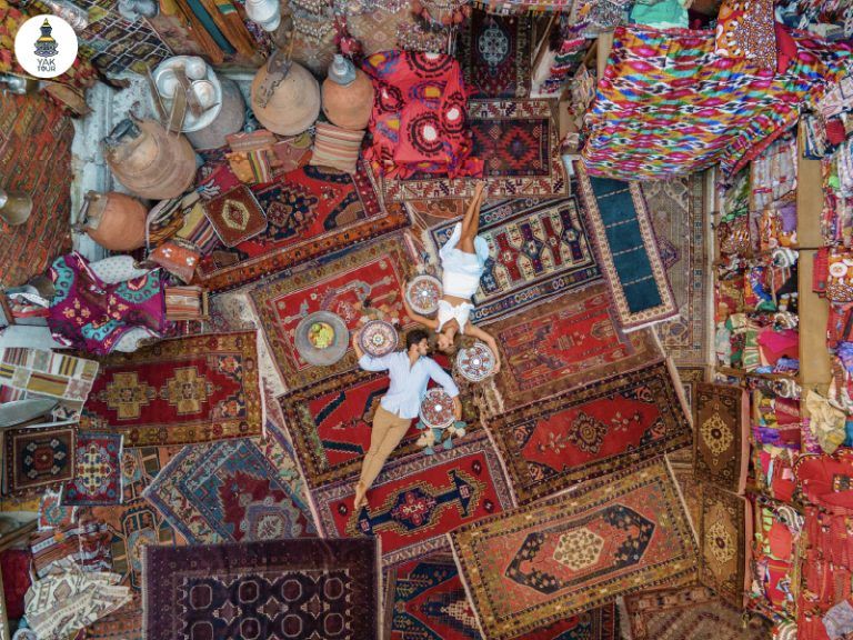 ภาพถ่ายมุมสูงของนักท่องเที่ยวท่ามกลางพรมพื้นเมืองลวดลายวิจิตรบรรจงในร้านขายพรม Galerie Ikman