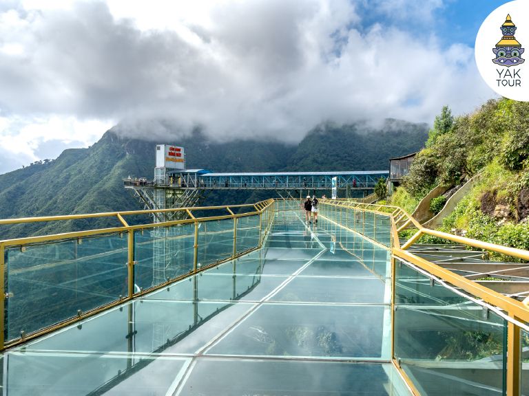 สะพานแก้วมังกรเมฆที่มีลิฟต์แก้วสูงตระหง่านริมหน้าผา พร้อมทางเดินกระจกใสทอดยาวให้นักท่องเที่ยวเดินชมวิวทิวทัศน์หุบเขาและทะเลหมอกในทริปเที่ยวซาปา