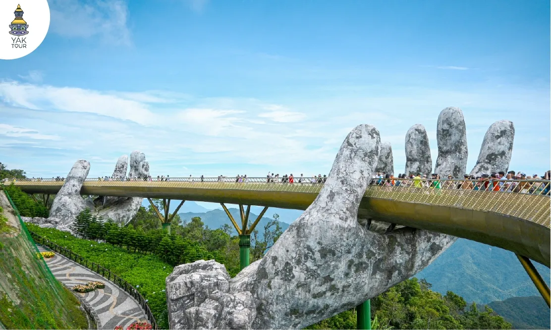 สะพานมือทองคำ (Golden Bridge) ดานัง แสดงโครงสร้างสะพานสีทองที่ถูกประคองโดยอุ้งมือหินยักษ์สองข้าง ท่ามกลางบรรยากาศภูเขาสูง ท้องฟ้าสดใส