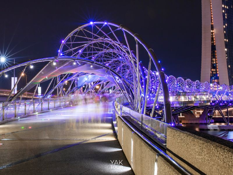 สะพานเฮลิกซ์รูปทรงเกลียว DNA ประดับไฟ LED สีม่วงยามค่ำคืนเหนืออ่าวมารีน่า