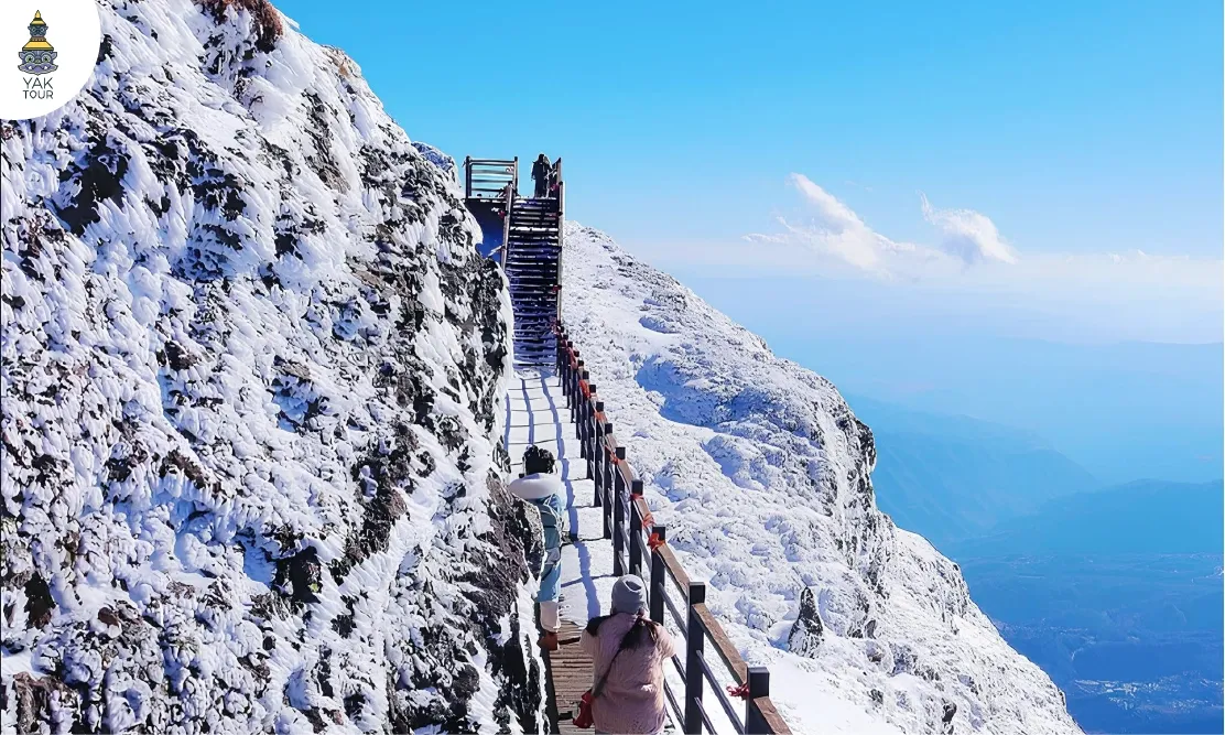 เส้นทางเดินสะพานไม้บนยอดภูเขาหิมะเจียวจื่อท่ามกลางหิมะขาวและท้องฟ้าใส