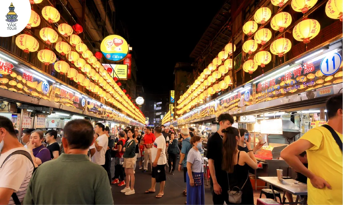 บรรยากาศความคึกคักของผู้คนและโคมไฟสีเหลืองนวลที่ประดับเรียงรายเหนือร้านอาหารใน Keelung Night Market เมืองจีหลง ประเทศไต้หวัน