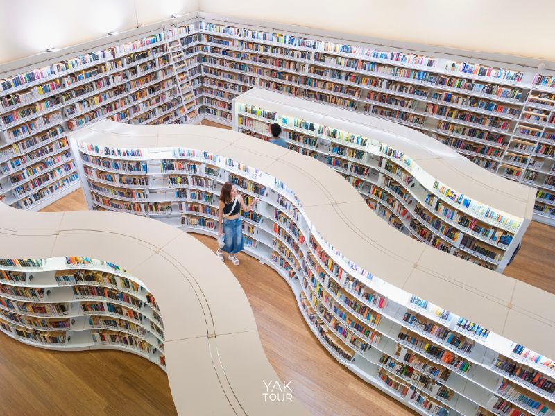 มุมสูงของชั้นวางหนังสือไม้ทรงโค้งมนที่เรียงรายอย่างมีดีไซน์ในห้องสมุด Library@Orchard