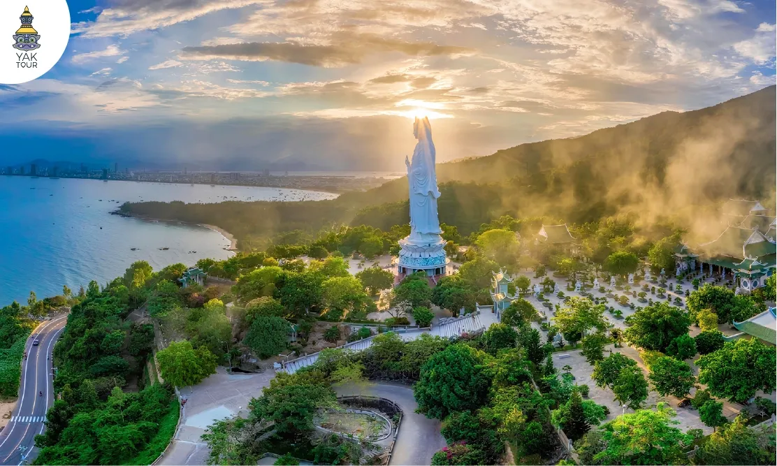 ภาพมุมสูง วัดหลินอึ๋ง (Linh Ung Temple) ดานัง แสดงองค์เจ้าแม่กวนอิมสีขาวสูงตระหง่านตั้งโดดเด่นท่ามกลางทิวทัศน์ธรรมชาติอันงดงาม บนเขาริมทะเลที่เขียวขจี