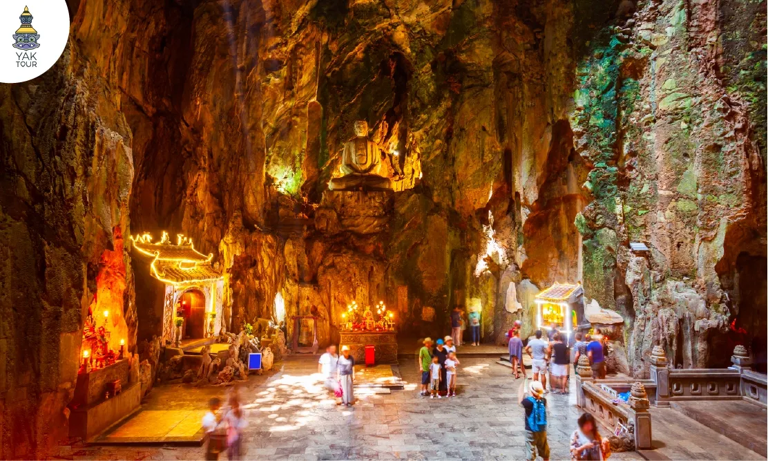 บรรยากาศภายในถ้ำของภูเขาหินอ่อน (Marble Mountains) ดานัง แสดงรูปปั้นพระพุทธรูปและศาลเจ้าประดับไฟสวยงาม ท่ามกลางลำแสงธรรมชาติที่ส่องลงมาจากเพดานถ้ำลงสู่พื้นหิน