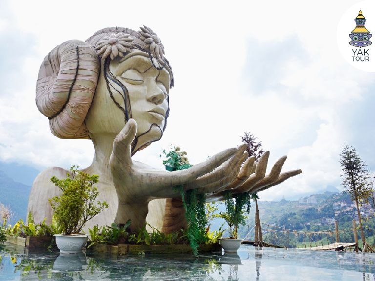 รูปปั้นผู้หญิงขนาดใหญ่หรือรูปปั้นโมอาน่าในท่าทางยกมือขึ้นสู่ท้องฟ้า ตั้งอยู่ท่ามกลางวิวภูเขาและสายหมอกที่โมอาน่าคาเฟ่ เมืองซาปา