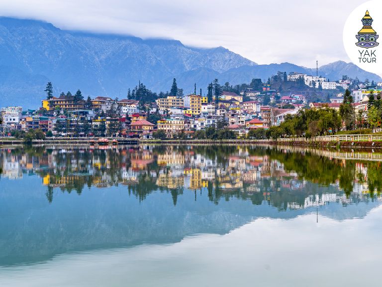 ทัศนียภาพอันเงียบสงบของทะเลสาบซาปาที่สะท้อนเงาอาคารบ้านเรือนหลากสีสันและเทือกเขาฟานซีปันบนผิวน้ำที่เรียบนิ่งดุจกระจก ภายใต้บรรยากาศเมืองพักผ่อนสไตล์ยุโรป