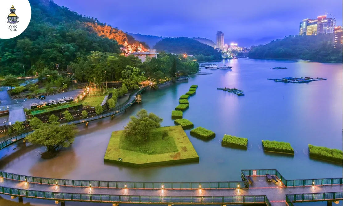 ทัศนียภาพทางเดินริมน้ำและขุนเขาโอบล้อมทะเลสาบสุริยันจันทรายามค่ำคืน