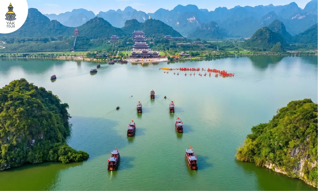 วิวมุมสูงของขบวนเรือนำเที่ยวกลาง ทะเลสาบตามจุ๊ก (Tam Chuc Lake) พร้อมทัศนียภาพภูเขาและสถาปัตยกรรมริมน้ำ