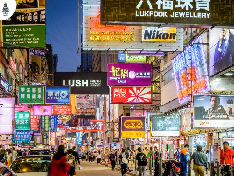บรรยากาศยามค่ำคืนในย่านจิมซาจุ่ยที่เต็มไปด้วยป้ายไฟนีออนของร้านค้าและห้างสรรพสินค้าสองข้างทาง