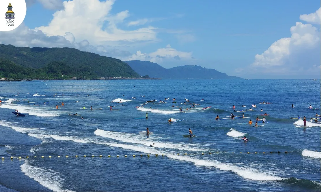 กลุ่มคนเล่นเซิร์ฟโต้คลื่นกลางทะเลสีครามที่ชายหาดไว่อ้าว